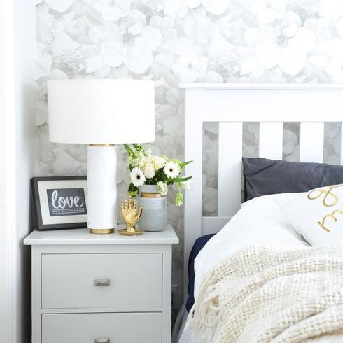 New Primary Bedroom A bedroom with floral wallpaper, a white bed and gray night stand.