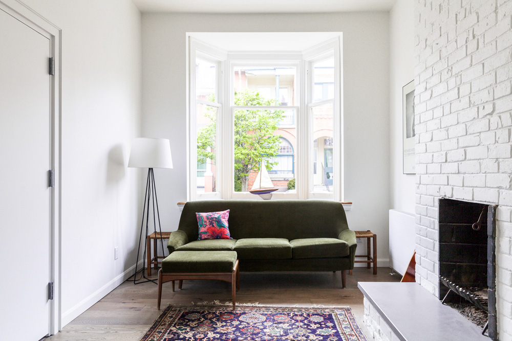 Green Spaces green velvet sofa in front of bay window in white room