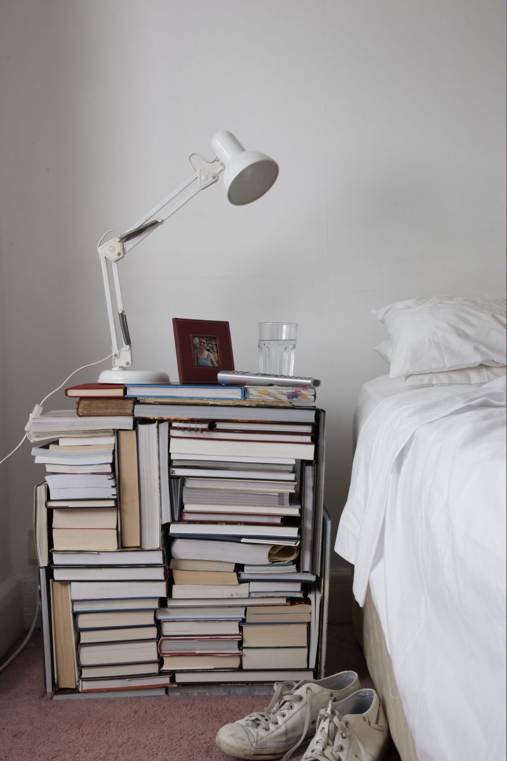Use Books as a Nightstand Books of various sizes are stacked together to create a makeshift nightstand.