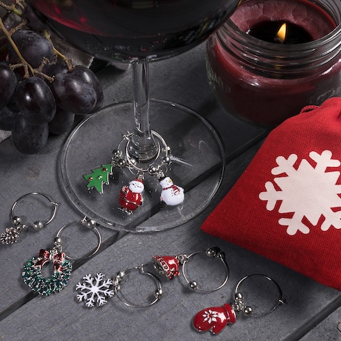 Clean as You Go Dainty holiday-themed wine charms are placed at the bottom of a wine glass and on the top of a table.