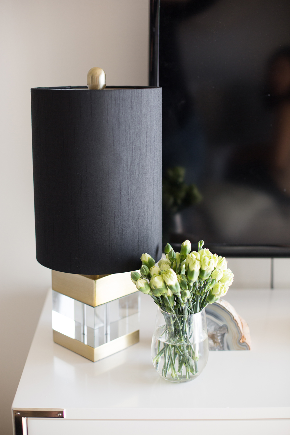 Little Luxurious Accents Black, gold and lucite lamp on dresser with small vase of carnations