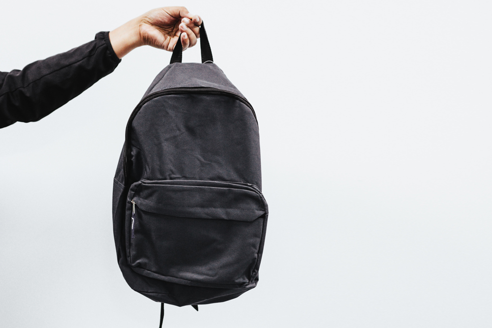 Do and Don’t: Backpacks and Lunch Bags person holding dark backpack in the air