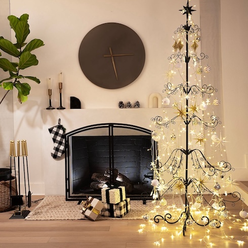 Prioritize a Cohesive Colour Palette A black decorative metal Christmas tree covered in lights, sitting in front of a sleek fireplace. Check-patterned gifts sit on the floor nearby.