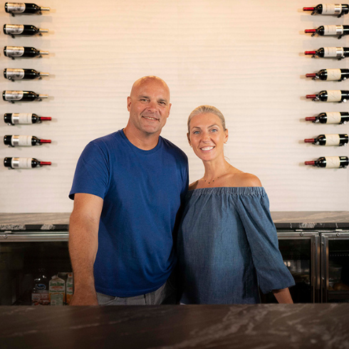 Is There an All-Inclusive Package? Bryan and Sarah Baeumler standing in front of decorate wall of wine bottles