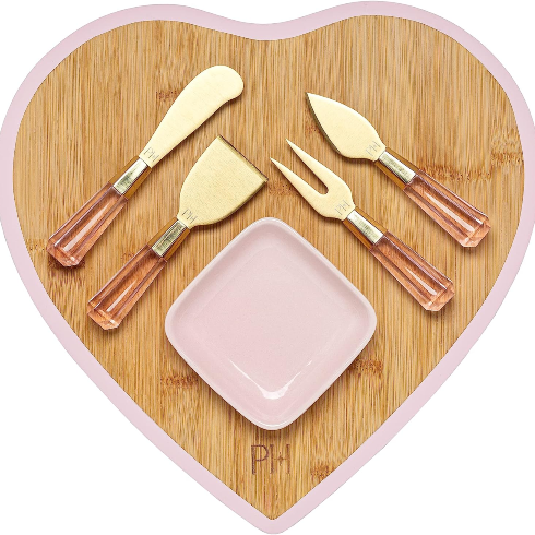 A Heart-Shaped Charcuterie Set A wooden pink-trimmed heart-shaped charcuterie board with gold and pink accessories