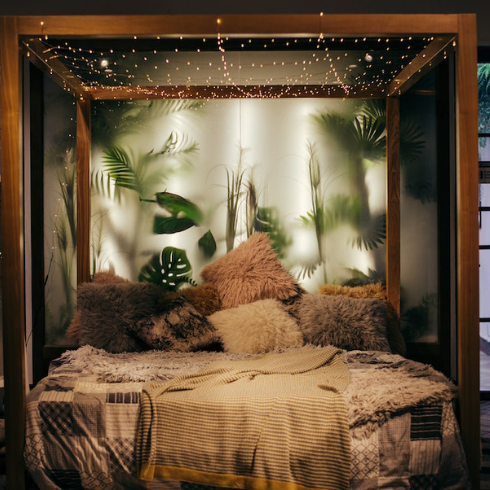 Perfectly Plush wood canopy bed with plush pillows in bedroom with plants behind frosted glass