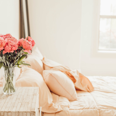 An Electronics-Free Oasis white bedroom with white bed and pink flowers on bedside table