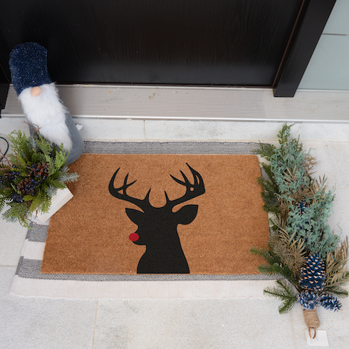 Embrace a Warm Welcome A silhouette of a red-nosed reindeer sits on a brown welcome mat outside a black front door of a home.